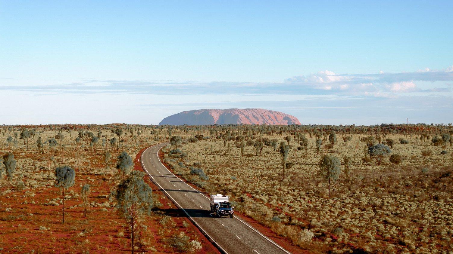 car with campervan driving away from Uluru
