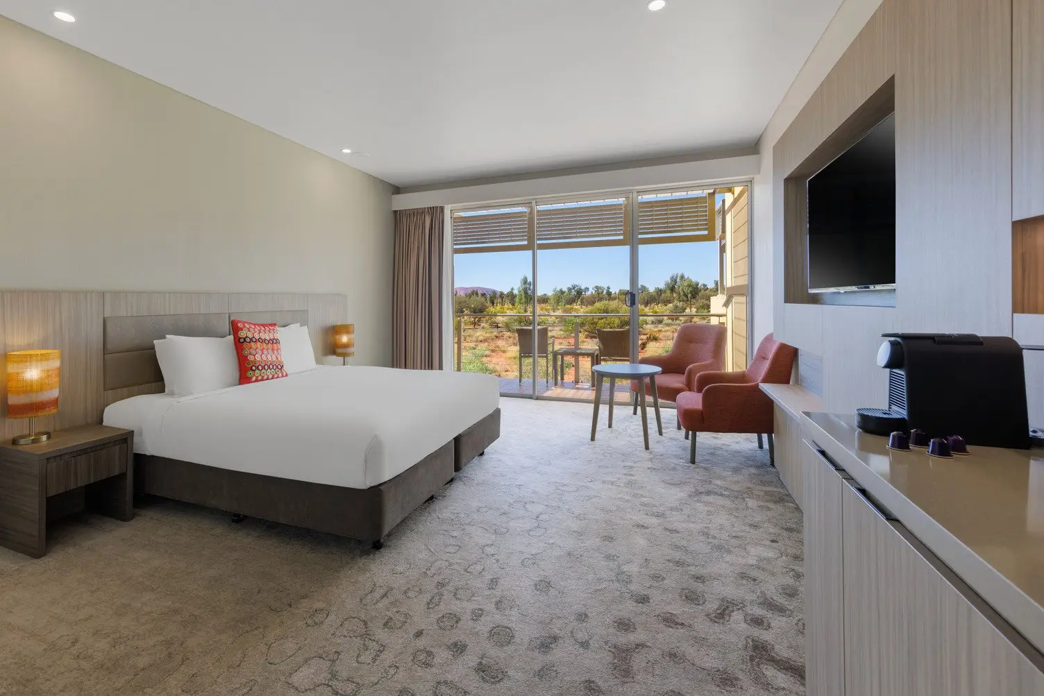 Desert Deluxe Room with a queen bed, two couches, TV and balcony over looking a view of Uluru