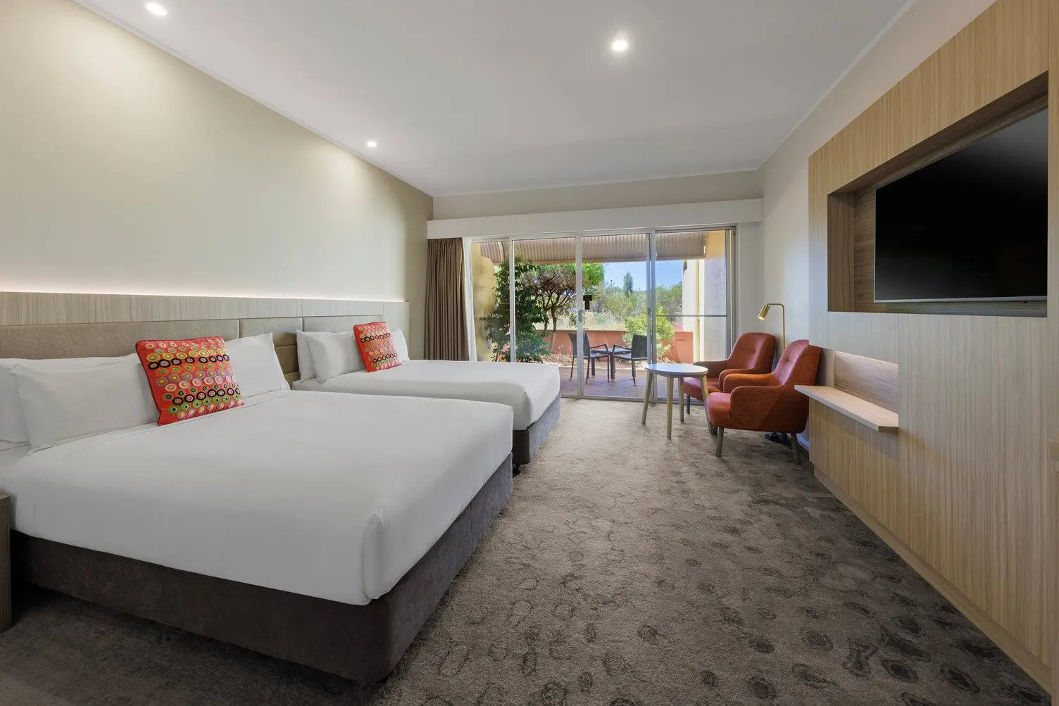 Two double beds with a TV mounted to the wall, two comfortable chairs and an outdoor area looking onto the desert lanscape