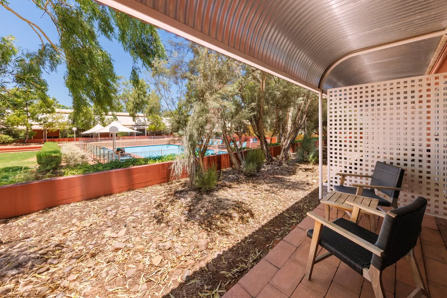 Outdoor area with two chairs and a table looking out towards the Desert Gardens pool with lots of native trees