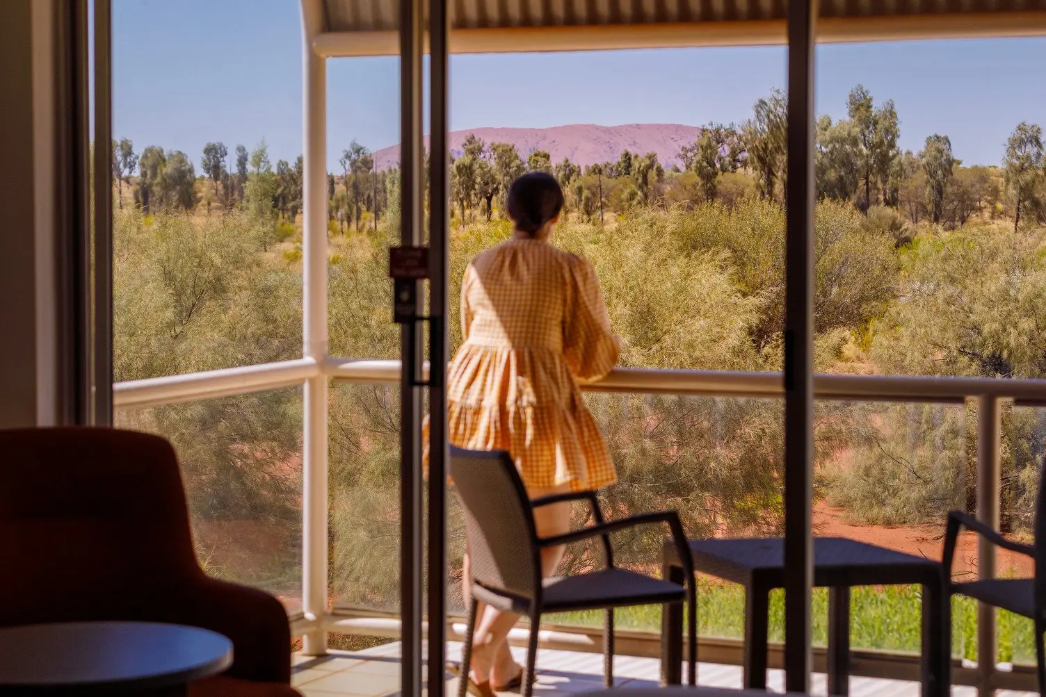 Ladystanding on the balcony looking out towards uluru and desert landscape