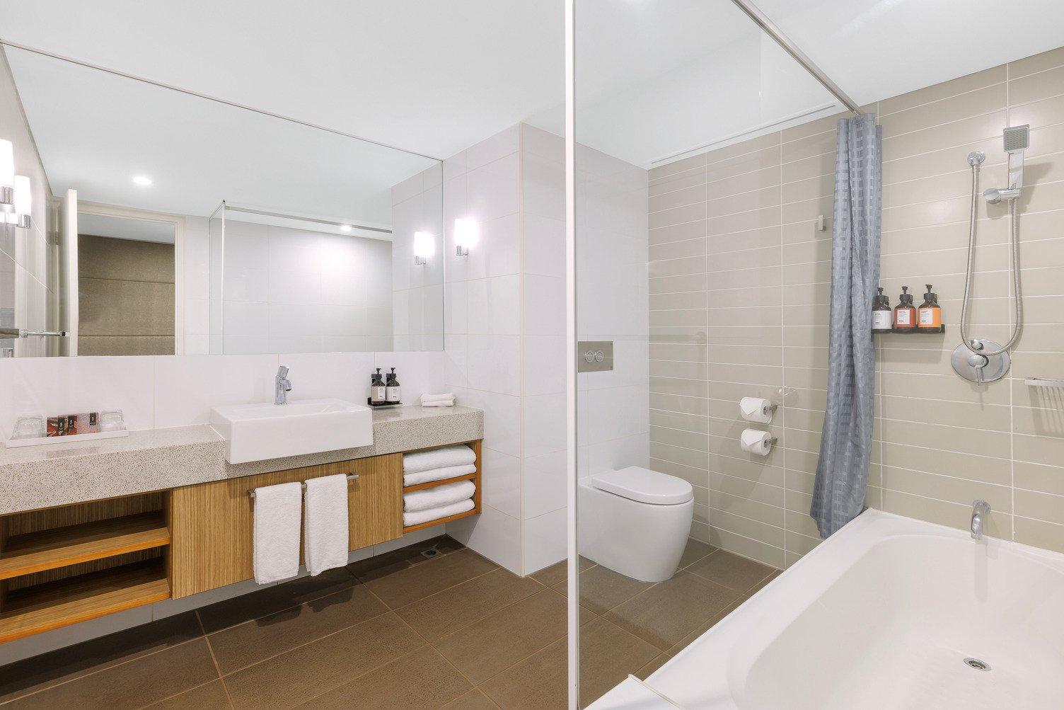 View of Bathroom with joined bathtub and shower, toilet, large mirror with benchtop, towels and a basin