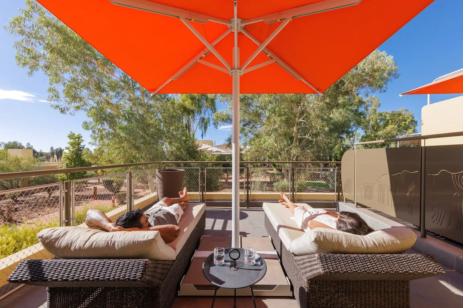 two people laying on sun lounges on balcony in Deluxe Suite at Sails in the Desert, Ayers Rock Resort