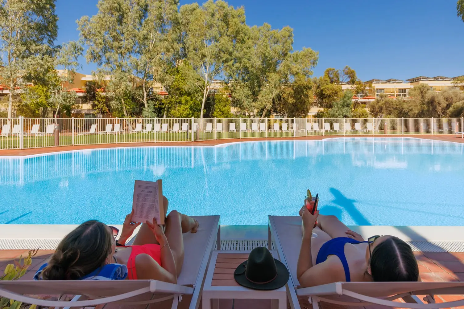 Two people laying on lounge chairs at the Sails in the Desert swimming pool