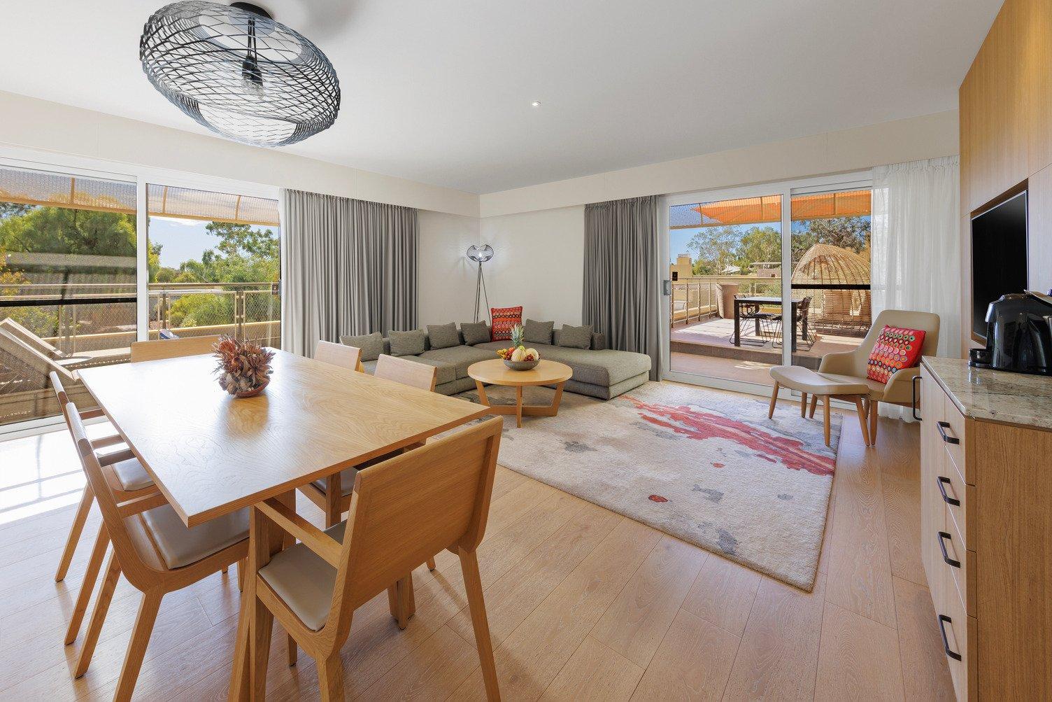 Suite with 6 table dining set, large rug with L shape grey lounge, TV mounted to the wall, looking onto a balcony with ourdoor lounge and chairs