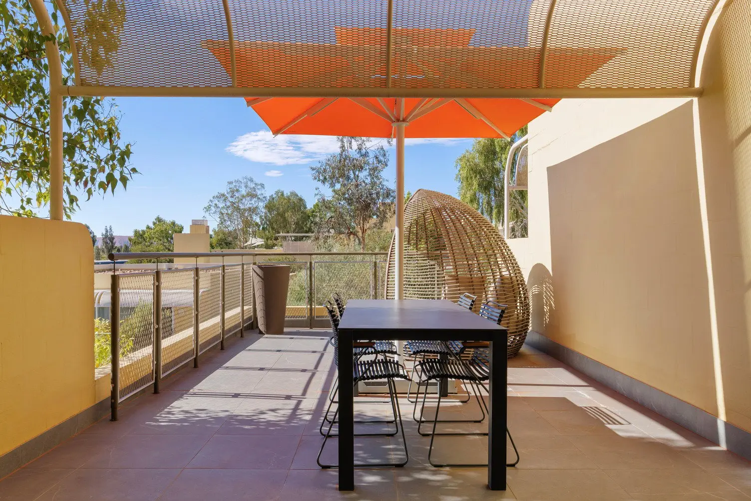 Balcony with 4 chair dining set with a large orange umbrella providing shade and a large egg chair at the end