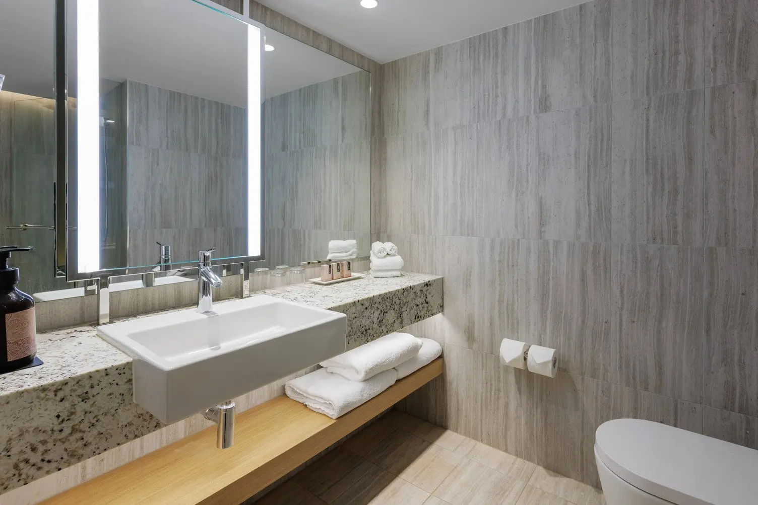 A modern bathroom with a sink, towels, toilet, large mirrors, complimentary Wiru shampoos and soaps