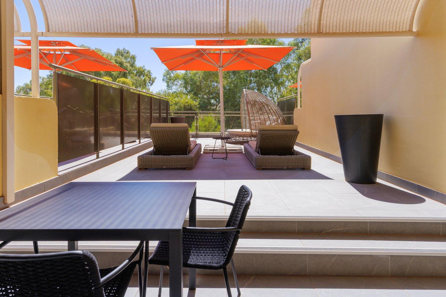 Balcony with outdoor dining table and chairs, and two sun lounges underneath a large orange outdoor umbrella