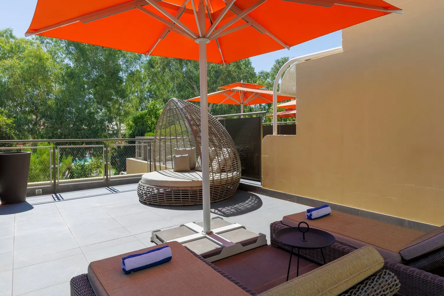 Balcony with two sun lounges underneath a large orange outdoor umbrella, and a large round egg chair with cushions