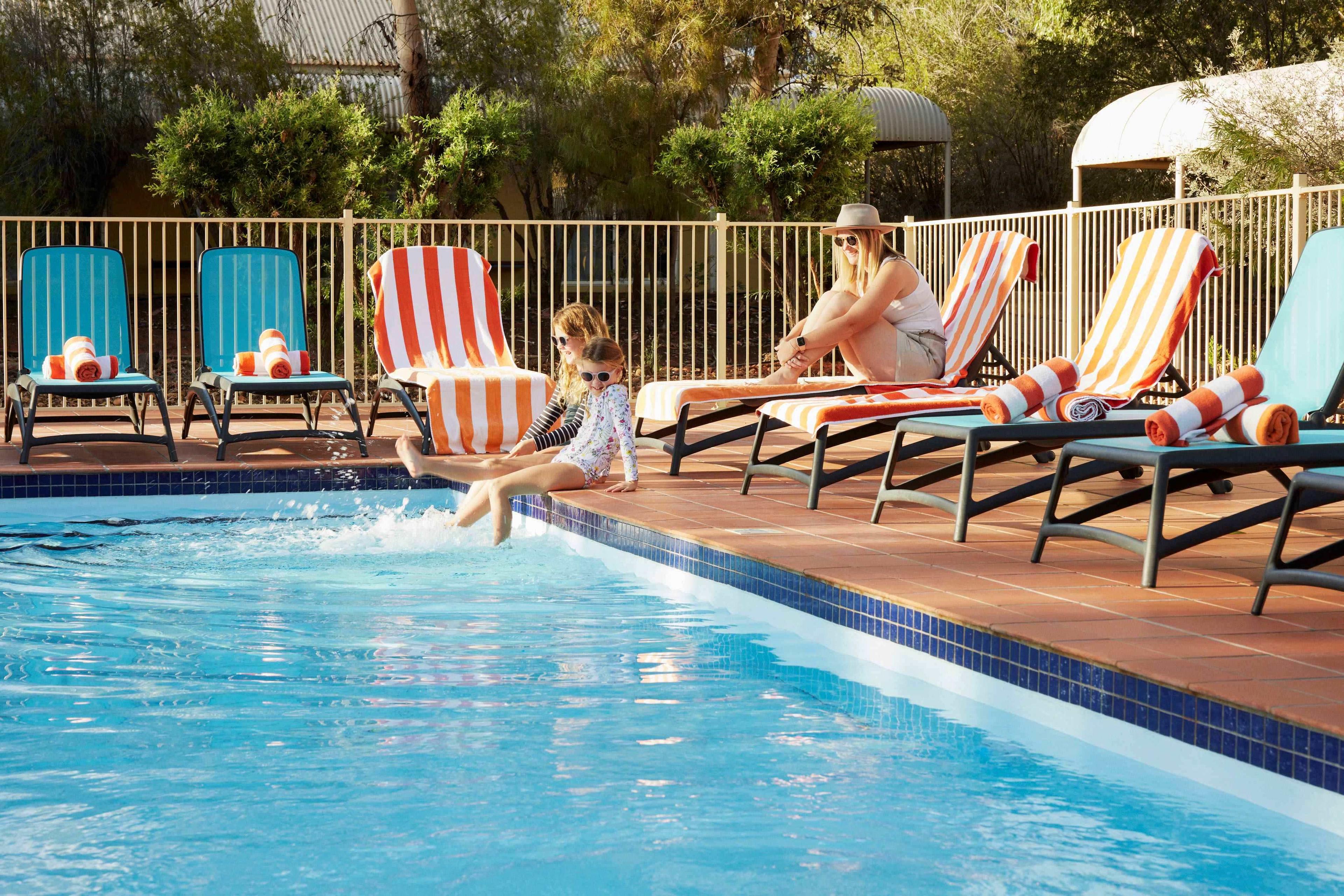 An image of a family sitting by the swimming pool and laying on a sun chair