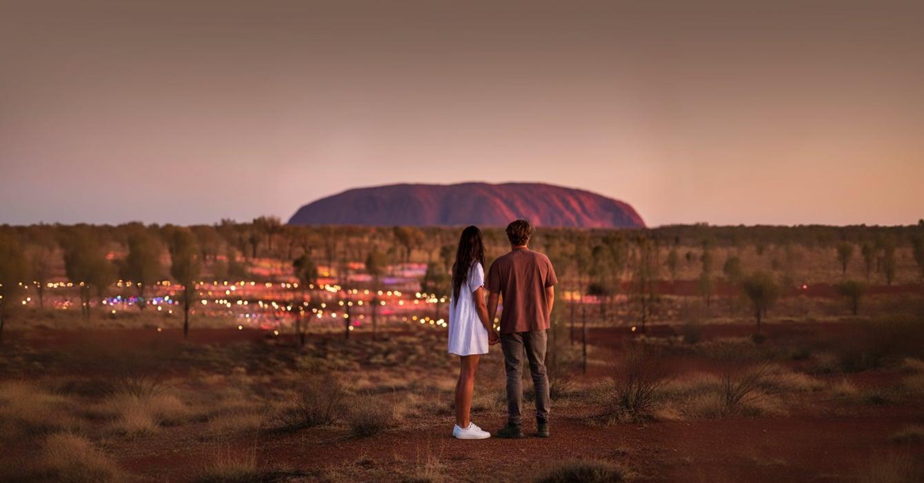 Couple standing in front of the Field of Light exhibition with Uluru in the background