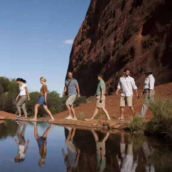 A group walks through the outback; people walking in line in the Uluru Australia near a lake