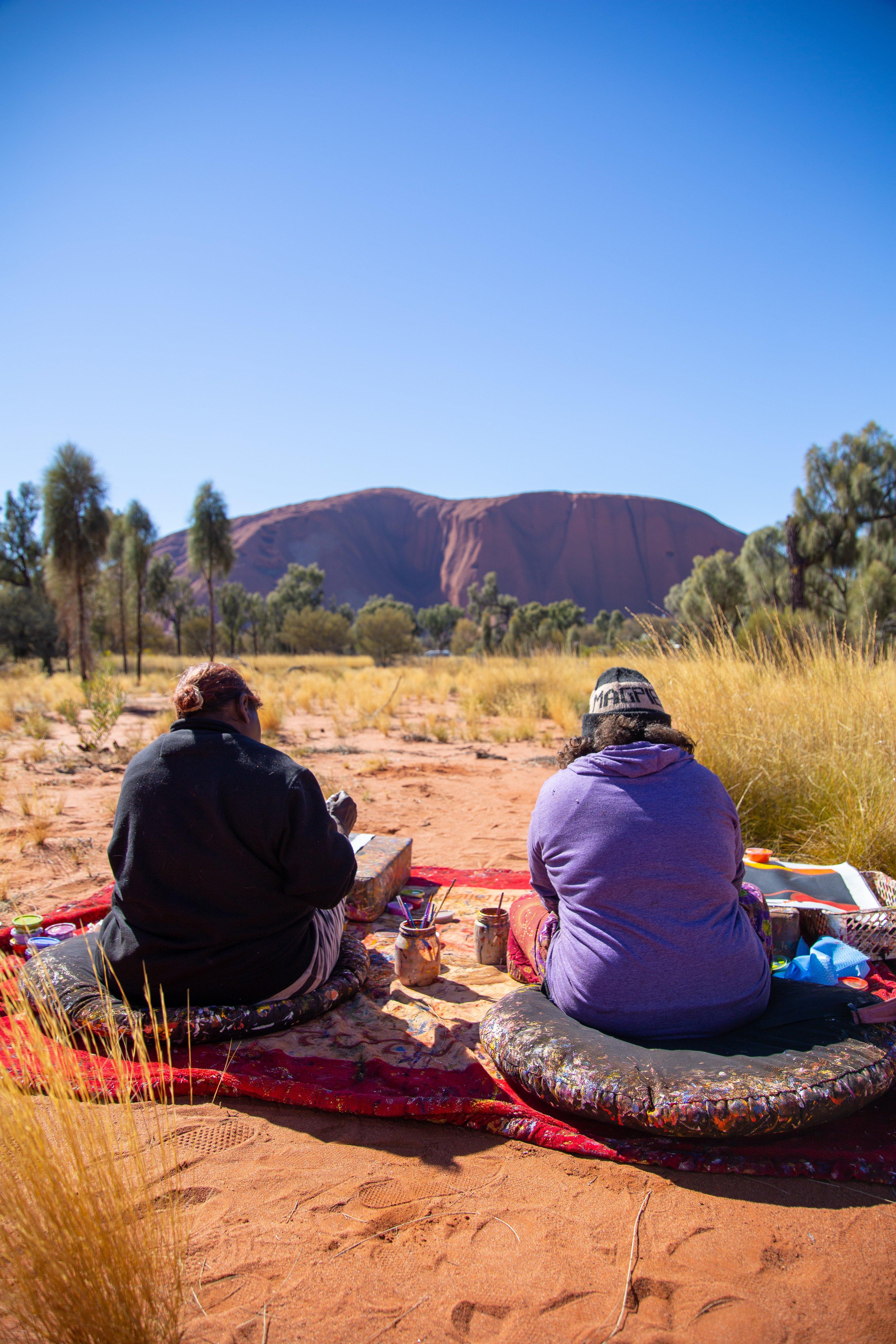 two people sitting on blankets in the outback