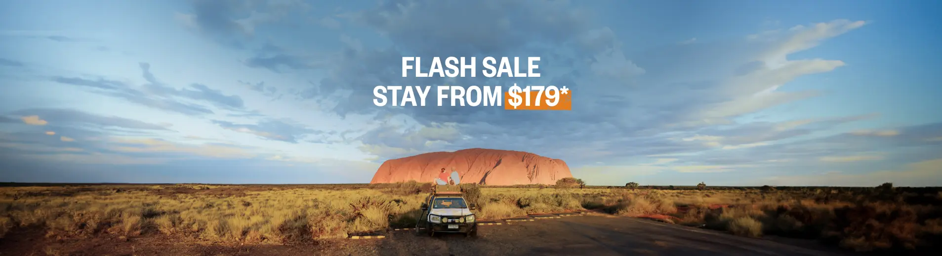 Two people sitting on top of a car looking over the Australian Outback and Uluru