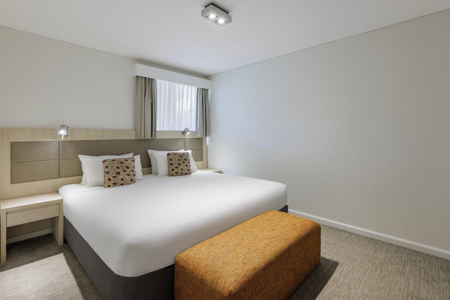 King bed with white sheets and a zipper at the end. Window at the top of the bed