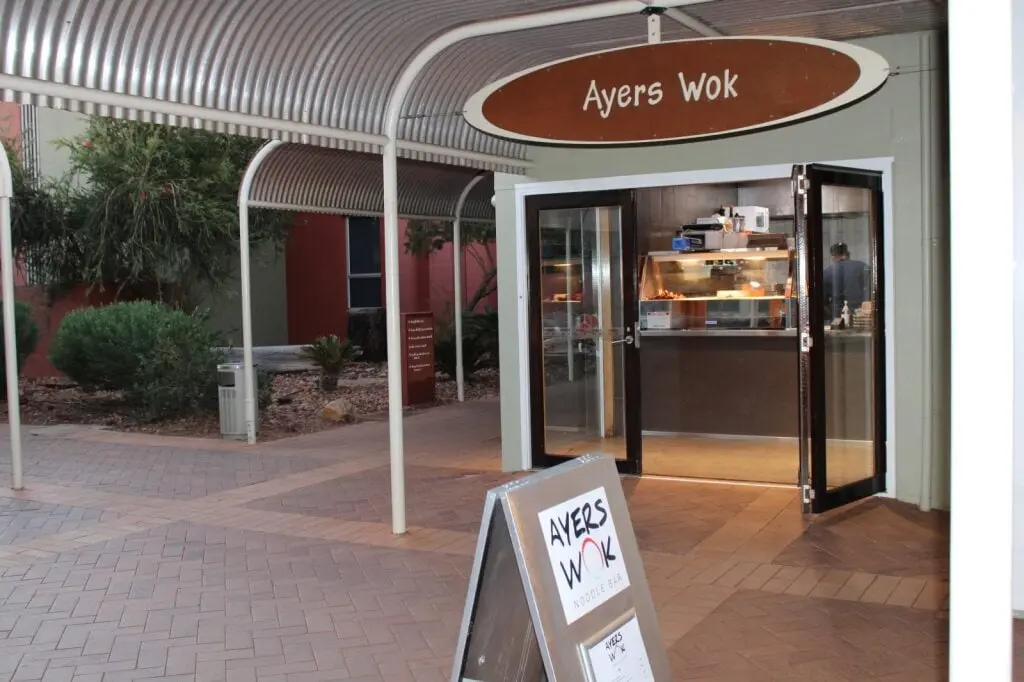 The front entrance of Ayers Wok with sliding doors open and a chef in the ktichen, with a sign outside,