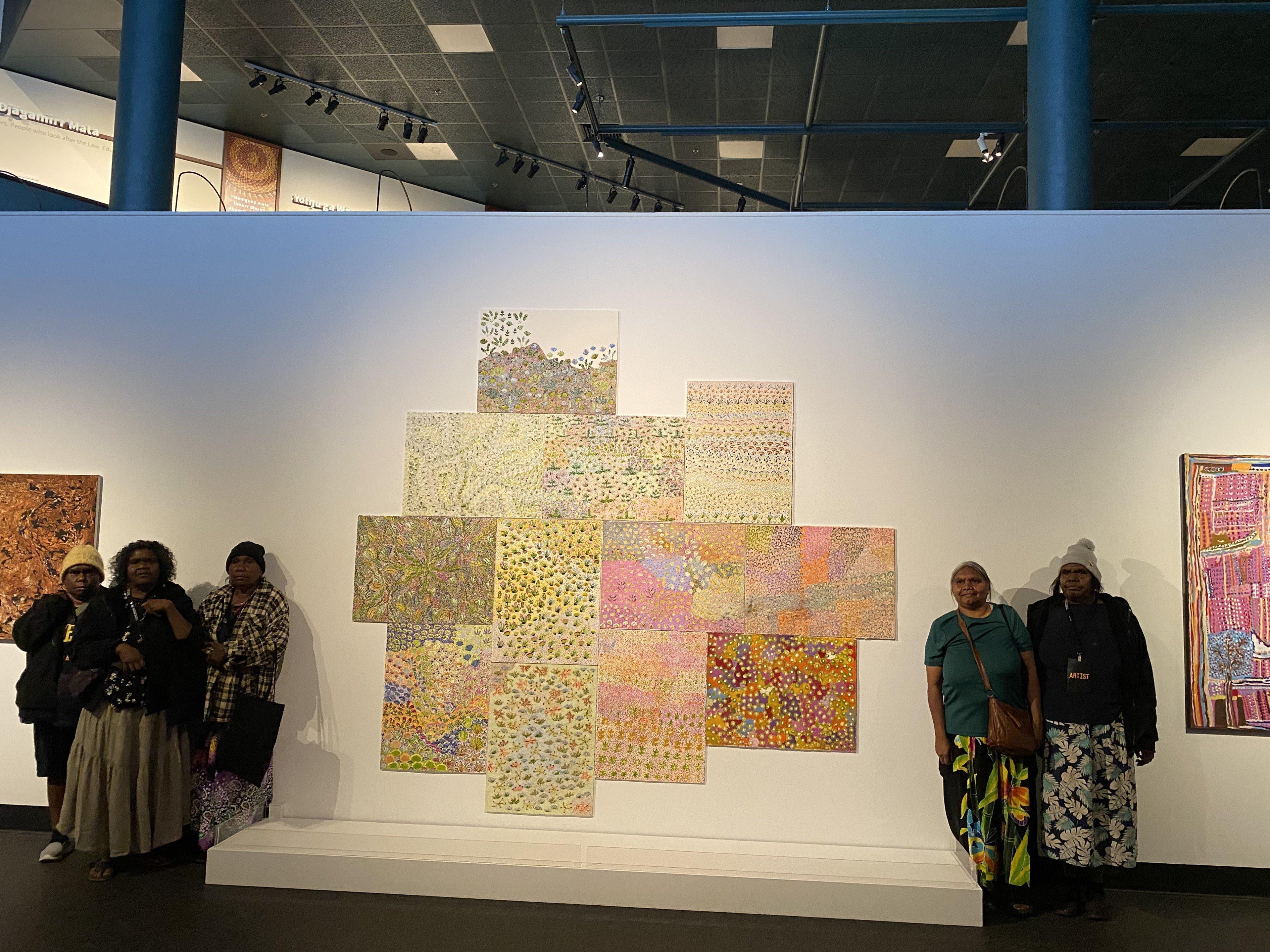 Artists of Ampiliatwatja standing in front of their artwork at an exhibition