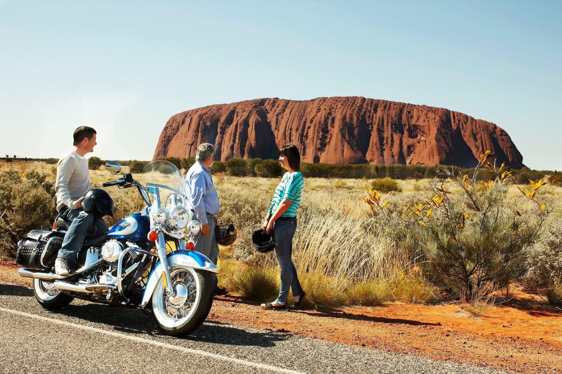 Motorcyclists meet up with a woman in view of Ayers Rock