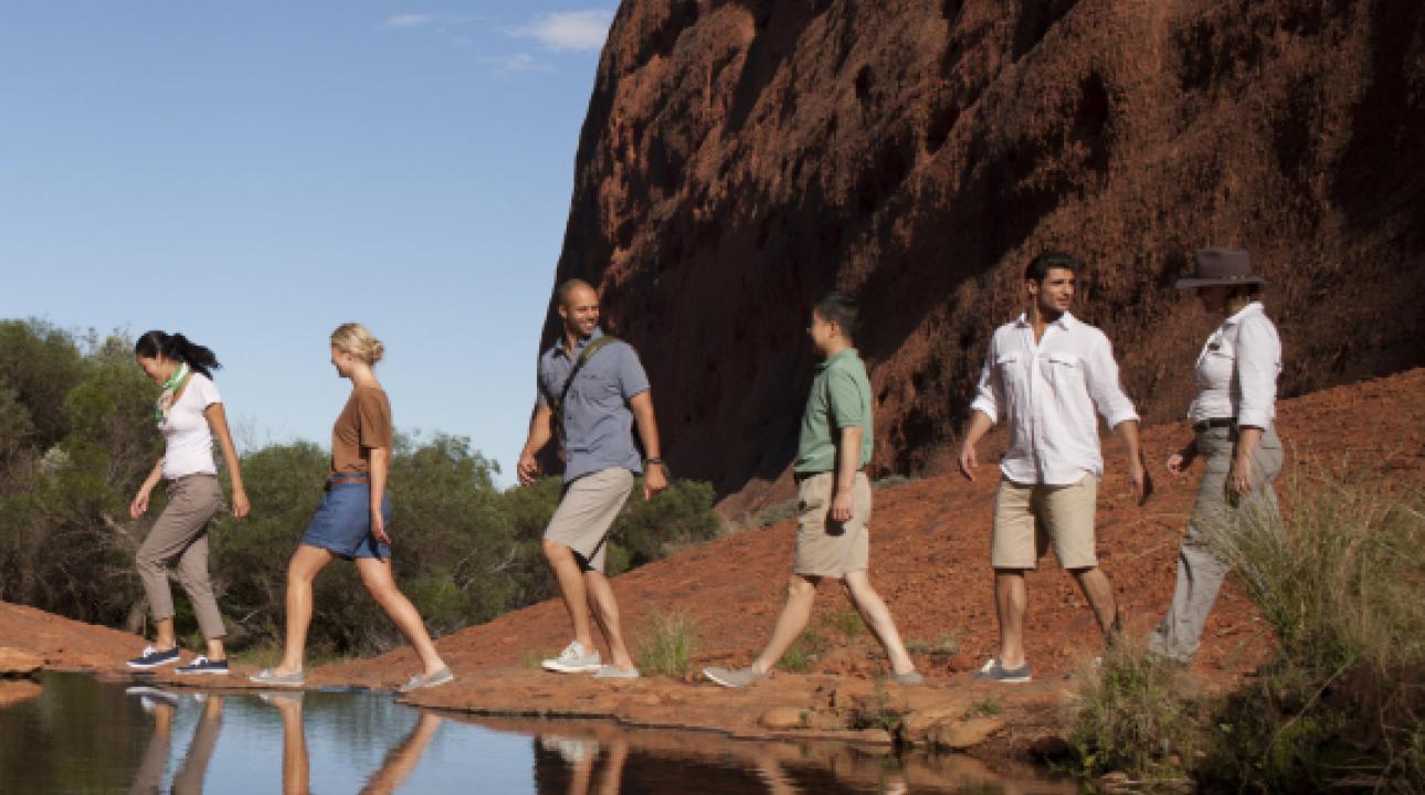 A group walks through the outback; people walking in line in the Uluru Australia near a lake